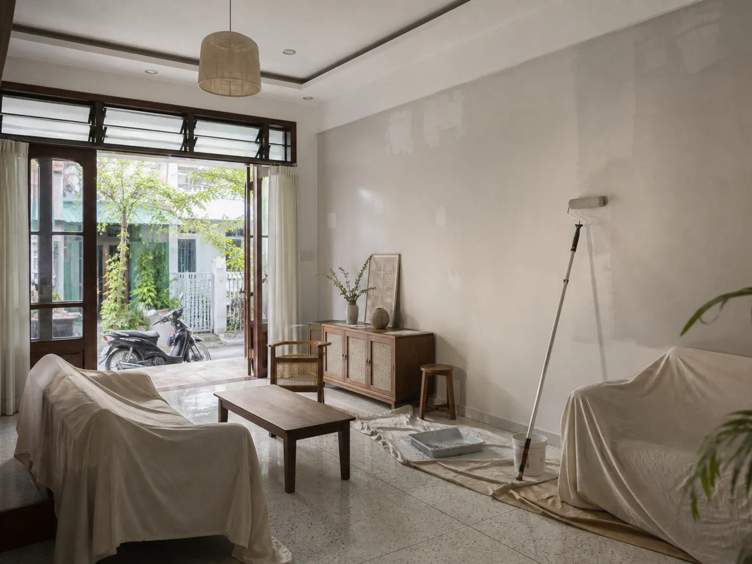 Phòng khách nhà phố Việt Nam đang sơn lại, nội thất được che phủ và tường cũ đã vá sửa